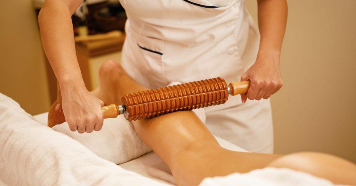 Unrecognizable therapist performing maderotherapy on woman's legs during massage treatment at the spa.